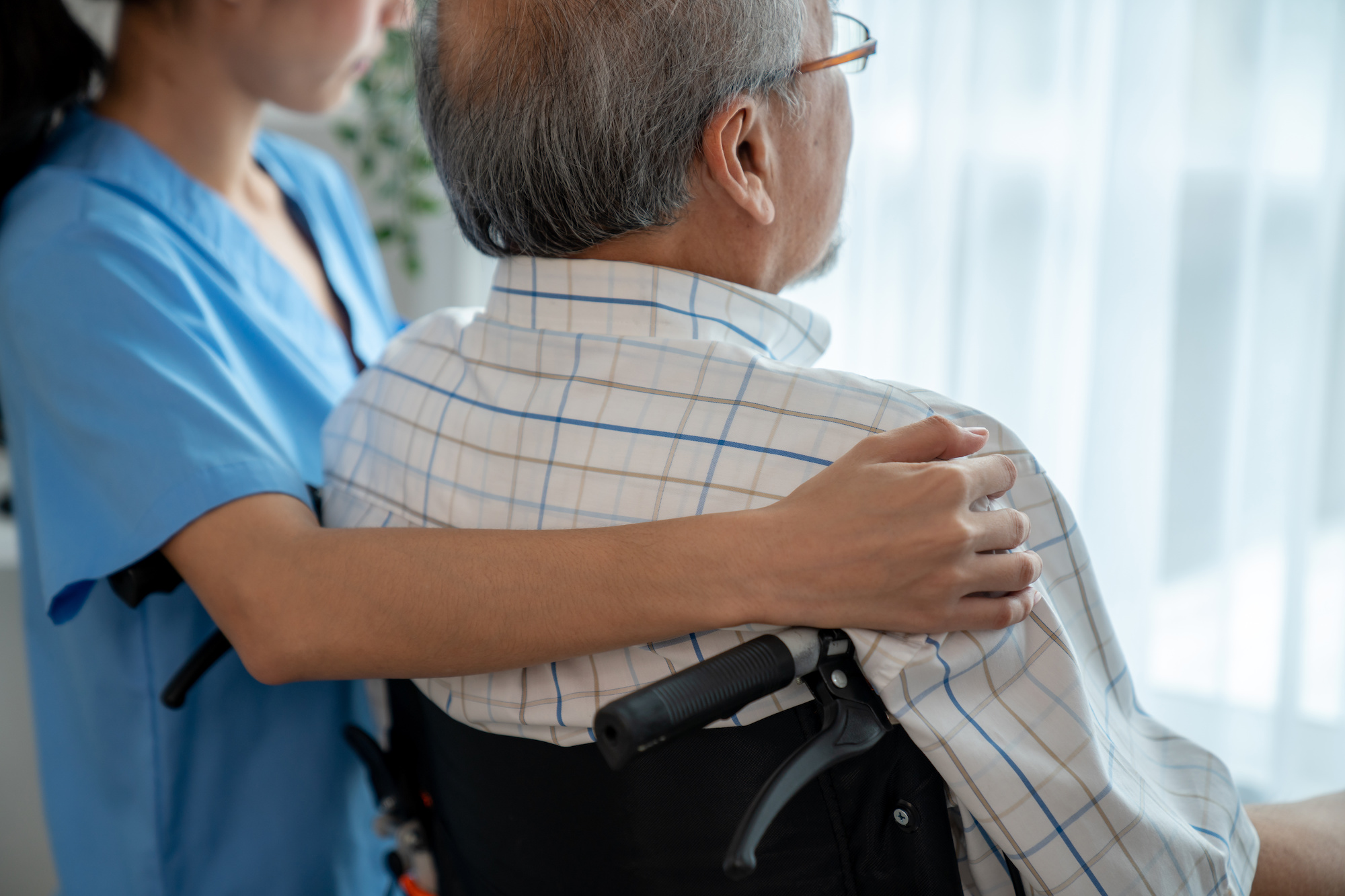 Rear view of a caregiver and her contented senior patient together in the room.
